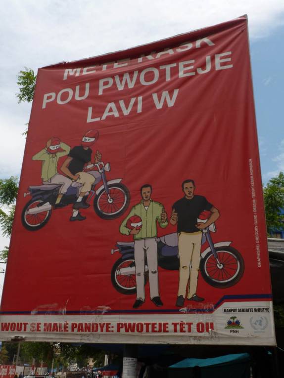 Solenemente ignorado, cartaz recomenda o uso de capacetes para motociclistas em Port-au-Prince, capital do Haiti